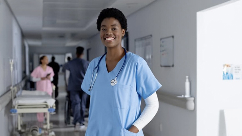 A smiling African American nurse stands in a hospital hallway