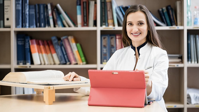 A nurse studies in a library using a textbook and her laptop