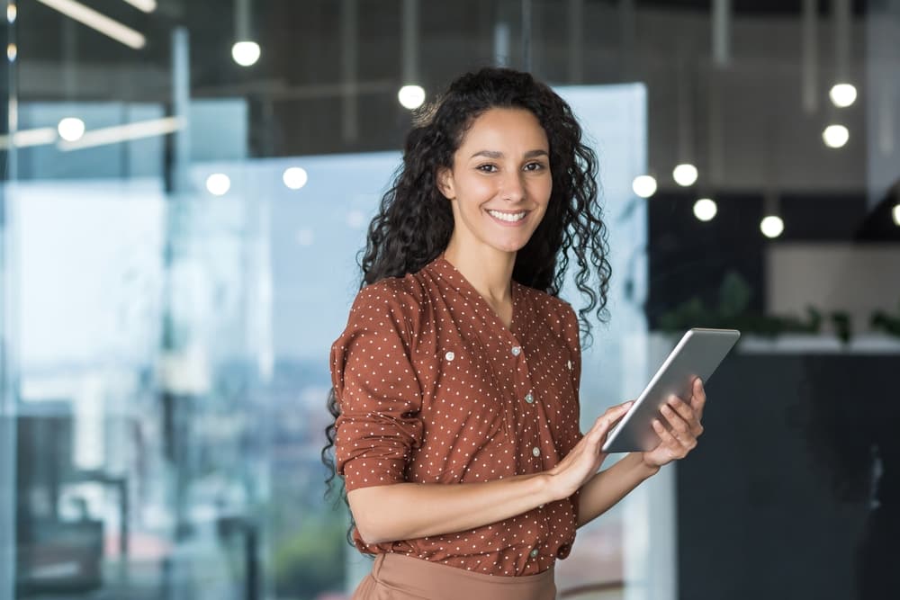 A smiling young professional works reviews information on her tablet.