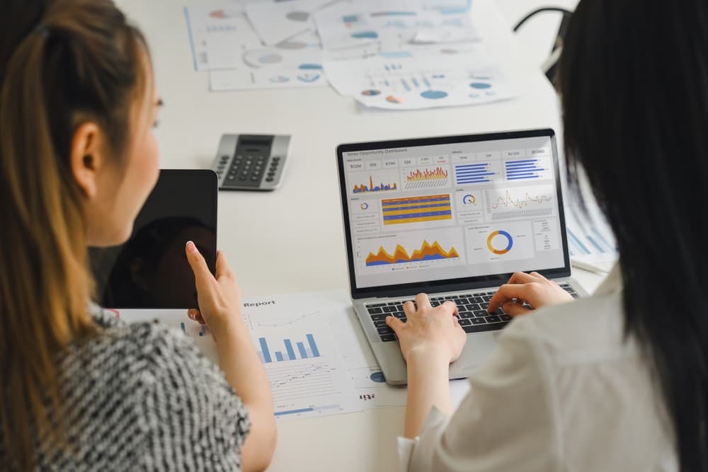 An overhead perspective of two businesswoman reviewing a KPI dashboard